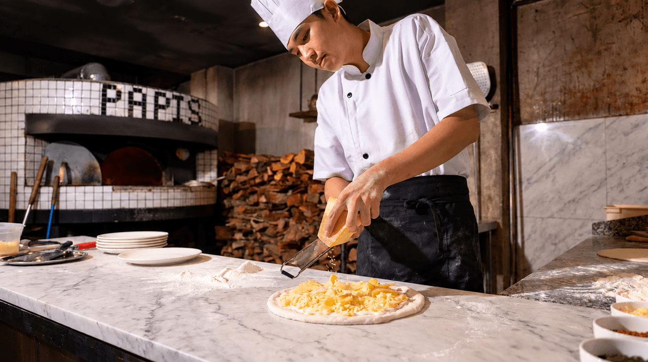 Đầu bếp PAPIS rắc phô mai lên bánh pizza trước lò nướng củi